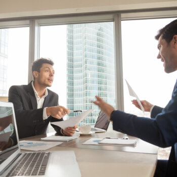 Two company partners disputing while pointing at documents.